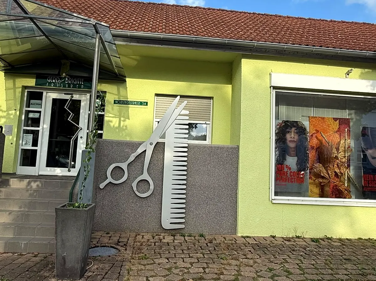 Die große Schere und der Kamm aus Metall an der Fassade von Gerd + Brigitte Frisuren.